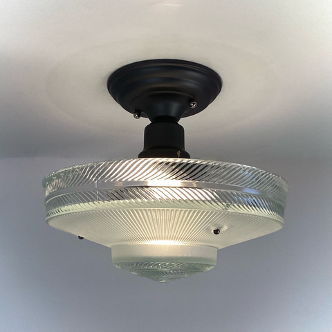 Vintage pressed-glass saucer ceiling light glowing, matte black canopy; three-chain mount. Vintporium