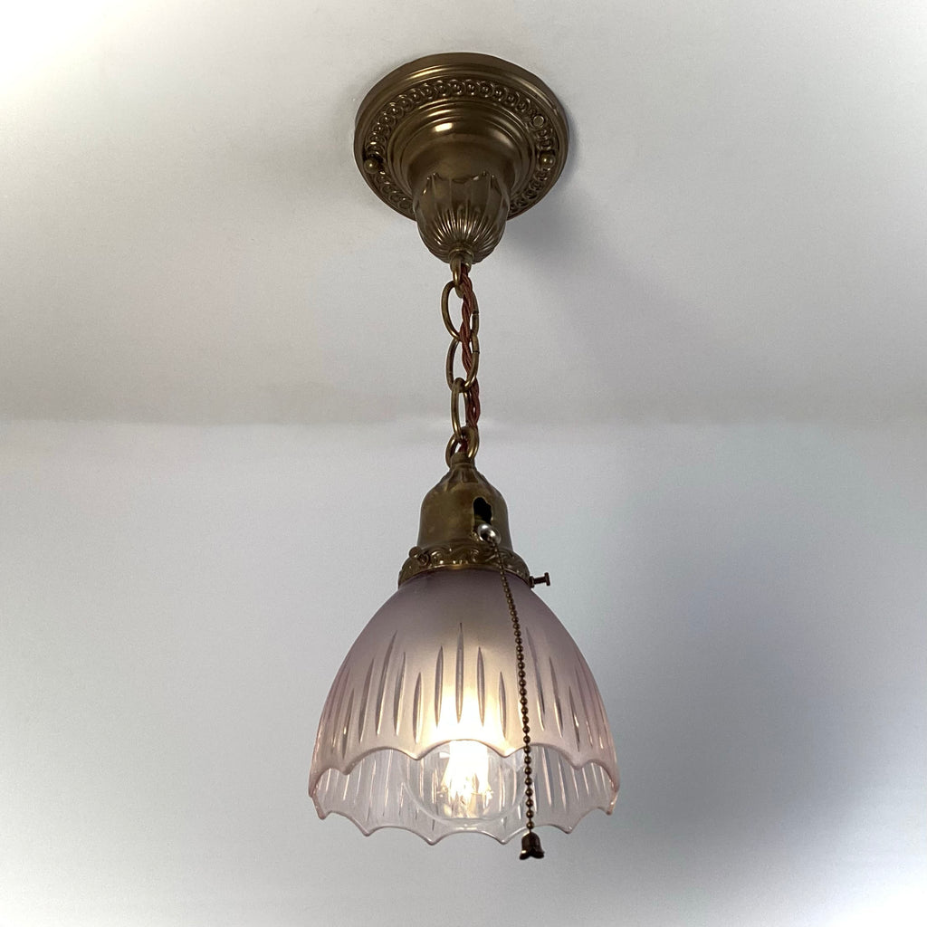 1920s antique brass pendant light with frosted fluted glass shade and pull-chain, hanging from ornate canopy.