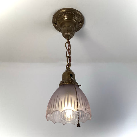 1920s antique brass pendant light with frosted fluted glass shade and pull-chain, hanging from ornate canopy.