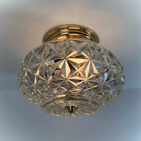 Mid-century crystal flush mount ceiling light fixture with diamond starburst glass shade and polished brass canopy, illuminated and photographed against a white ceiling — Vintporium.