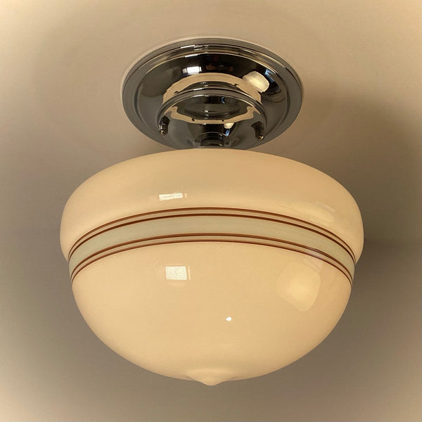 Vintage style schoolhouse flush mount light with polished chrome base and striped milk glass shade, warm lighting.