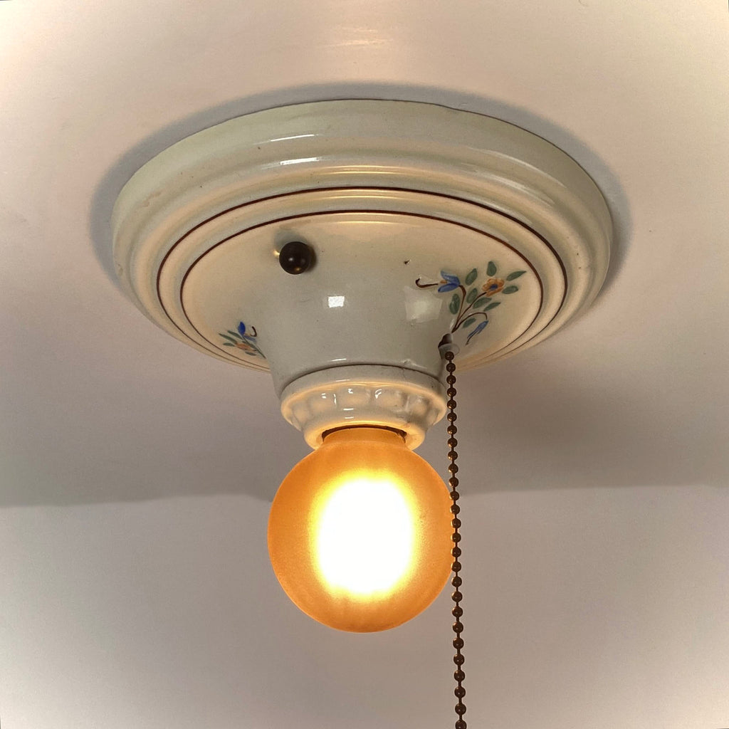 Vintage porcelain pull chain ceiling light with amber glass globe illuminated