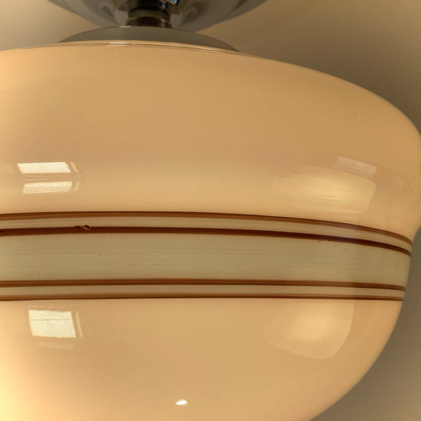 Close-up detail of brown and light blue stripes on a white milk glass light shade, warm lighting.