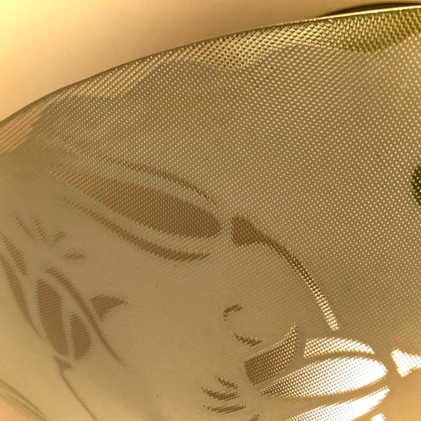 Detailed view of the warm glow passing through a textured, etched glass light shade with a floral pattern.