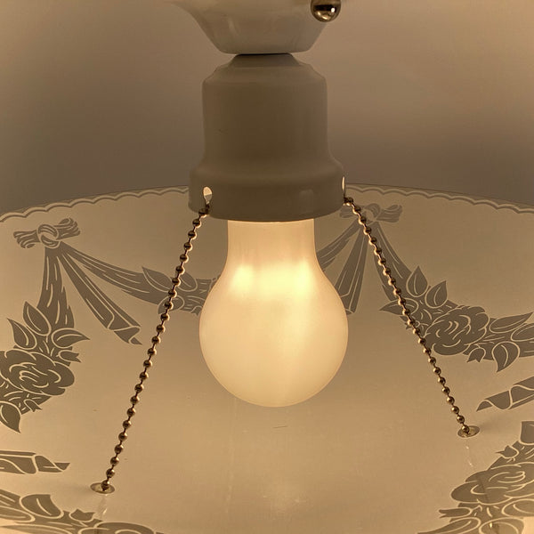 Pull-chain socket and bulb detail on a 1950s semi-flush ceiling light with enameled glass