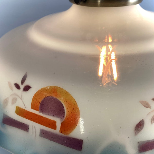 Detailed view of the colorful geometric motif and orange arches painted on a white milk glass shade.