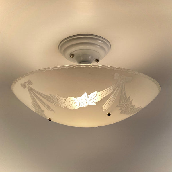 Lit 1950s semi-flush ceiling light showing enameled floral glass bowl glowing warmly