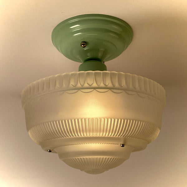 Art Deco–style semi-flush ceiling light lit, with frosted ribbed glass shade and period green canopy