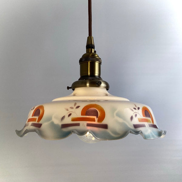 An Art Deco hanging light fixture showing the warm glow of the internal bulb through a opal glass shade.