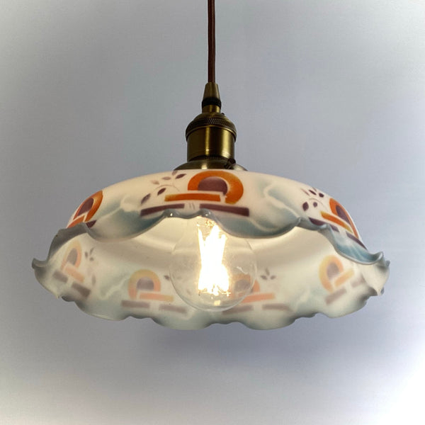 View from beneath an illuminated vintage glass pendant showing the warm interior light and ruffled glass rim.