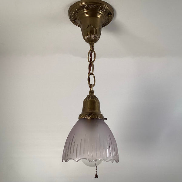 1920s antique brass pendant light with frosted fluted glass shade and pull-chain, hanging from decorative ceiling canopy.