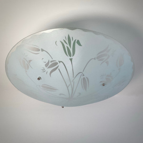 Wide shot of a frosted glass ceiling light shade with a green-tinted tulip motif against a white ceiling.