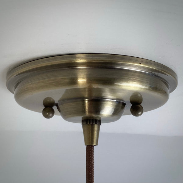 Detail of a circular antique brass ceiling canopy and a brown braided fabric electrical cord.